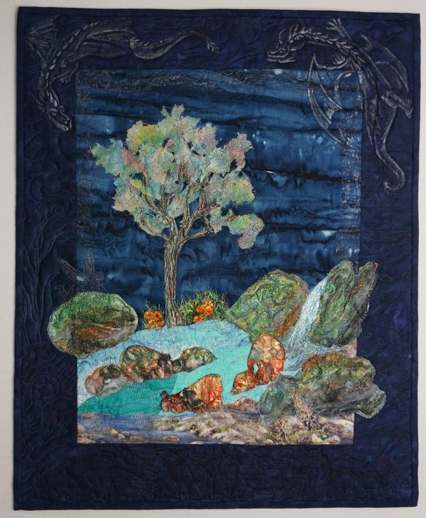 Karin Tauber - Dreaming of Dragons (a quilt landscape showing a tree, river and rocks. Stitched dragons fly around the dark indigo border.)